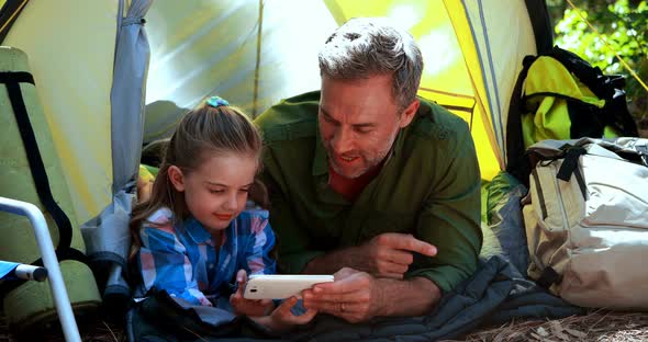 Father and daughter using mobile phone outside tent alt