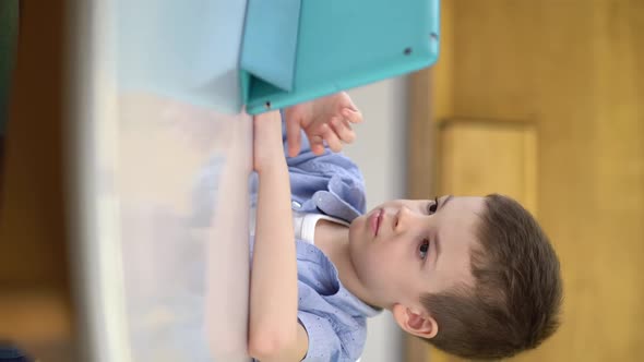 Preschooler Sits at a Table and Looks at a Digital Tablet alt
