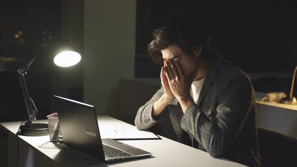 Male Programmer Who Works at a Computer at Night Rubs His Eyes From Fatigue and Lack of Sleep