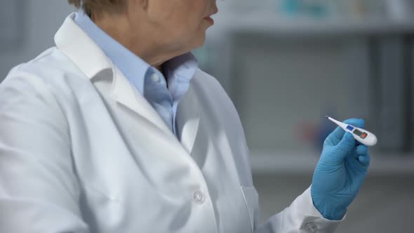 Female Medic Looking at Electronic Thermometer Indicator and Consulting Patient