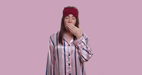 Young Bored Female in Pajamas Yawn and Shows Confusion Sign, Isolated Over Pink alt