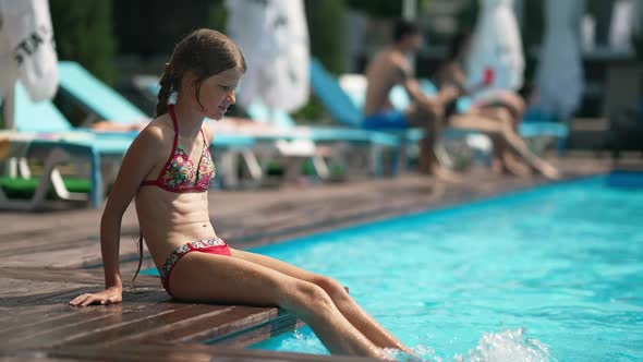 Side View of Little Girl Splashing Blue Water in Swimming Pool with Legs in Slow Motion alt