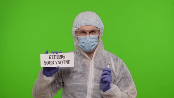 Medical Worker Doctor in PPE Suit with Syringe Ampoule Text Slogan on Paper Getting Your Vaccine alt