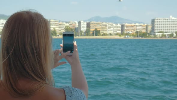 Woman with cell shooting sea and city from ship alt