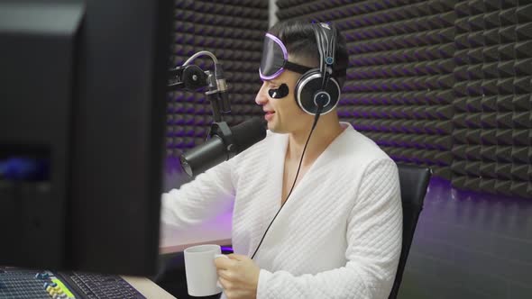 Radio Dj in Sleep Mask and Cosmetic Patches Drinking Coffee on Broadcast alt