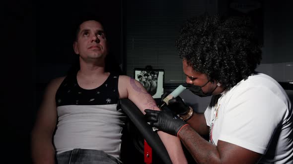 Professional African American Tattoo Artist Makes a Tattoo on Client Arm alt