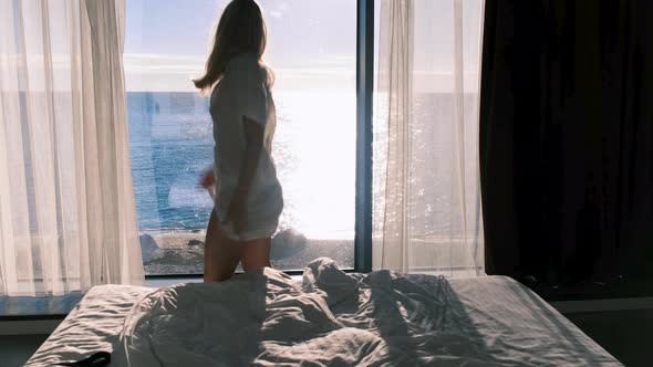 Woman in a Transparent Bathrobe Dances Against the Backdrop of a Panaramic Window Overlooking the alt