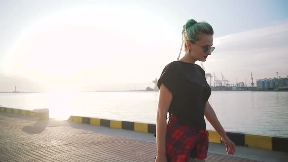 Young Stylish Funky Girl with Green Hair Riding Roller Skates and Dancing Near Sea Port During alt