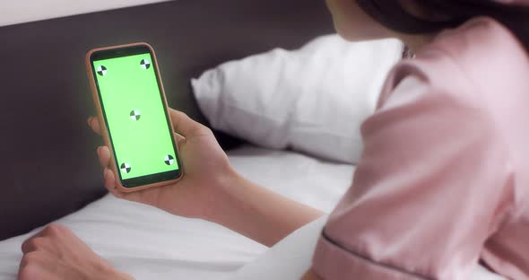 Woman Holds a Phone with a Green Screen in Her Hands While Lying in Bed