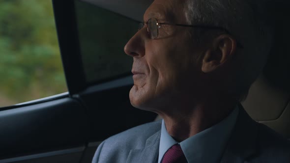 an Elderly Man in Glasses and a Suit Rides in a Car