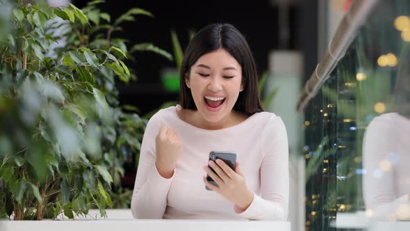 Asian Korean Girl User Freelancer Player Woman Sitting in Coffee Shop at Table in Office with Phone alt