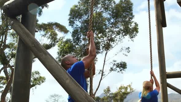 Fit man and woman climbing rope during obstacle course alt