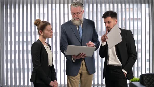 Mature gray-haired executive explains something to young employees of the firm alt