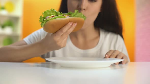 Young Female Biting Delicious Hot-Dog and Smiling, Lunch Break in Restaurant alt