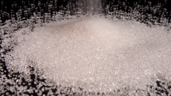Falling grains of sugar on a black mirror background. alt