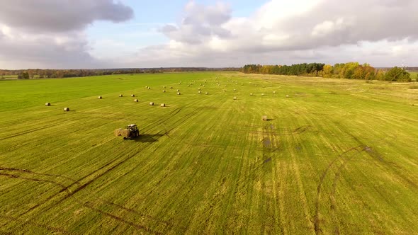 The tractor is stacking haystacks on an agricultural field in autumn, aerial view alt