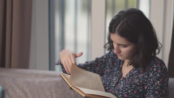 Brunette Girl Reading a Book While Sitting on the Sofa Window Background alt