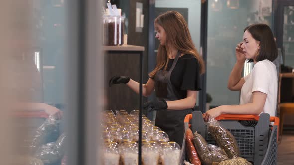 Woman Client Is Choosing Dried Fruits at the Store with a Female Seller alt