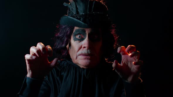 Frightening Senior Man with Halloween Witcher Makeup Trying to Scare Showing Black Dirty Tongue alt