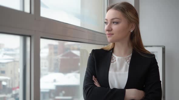 Serious Businesswoman in Black Suit Looking to Window in Modern Office alt