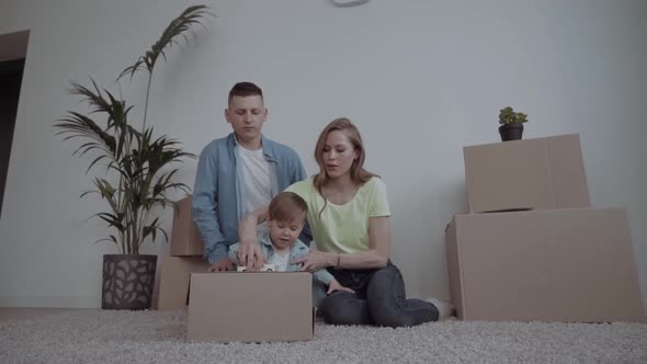 Image of Happy Couple with Children Sitting on Floor Among Cardboard Boxes alt