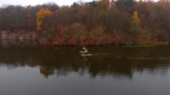 Drone Shot of Man and Woman on Sup Paddle Boards at Wide River on Golden Autumn Forest Background alt