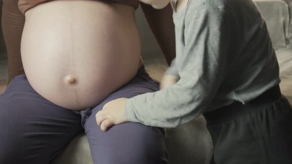 Pregnant Woman Sitting on Couch Little Boy Listens to Baby Movement in Belly alt