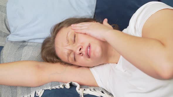 Young Woman Lies on the Bed with Her Eyes Closed and Massages the Temples of Head Due to Migraines