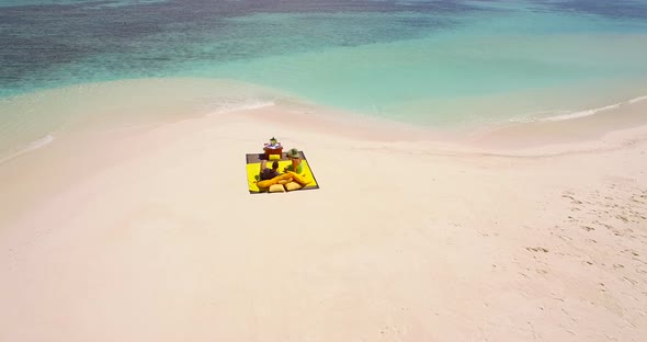 Aerial drone view of a man and woman couple having a picnic meal on a tropical island beach. alt