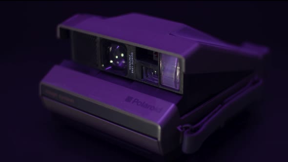 Vintage Polaroid Camera on a turntable with purple light and black background