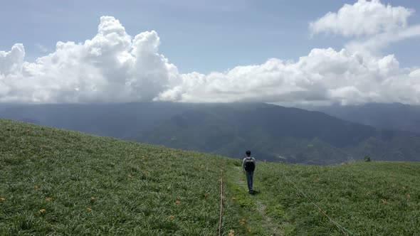 Aerial - Tracking shot and flyover young male walking on a grass mountain alt