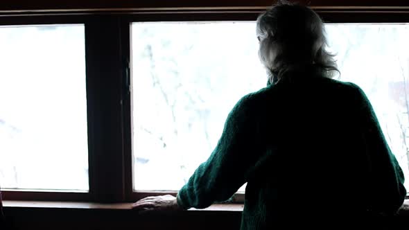 An Elderly Woman Stands By the Window and Turns to the Camera