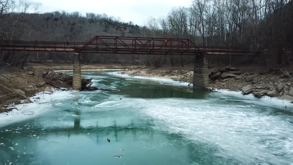 Drone Going Under Rusty Footbridge Over Icy River alt