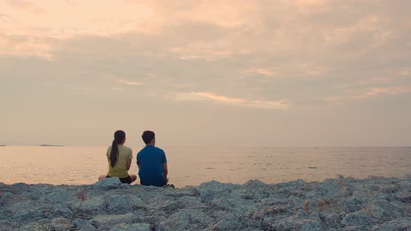 Young couple runner taking rest after running and sitting seaside looking at the beautiful sunset. alt