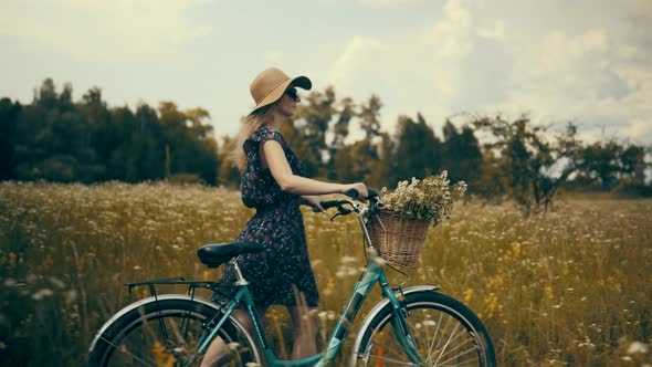 Woman In Hat Enjoying Weekend.Woman Cyclist Walking With Bike On Holiday Vacation Trip. Wildflower. alt