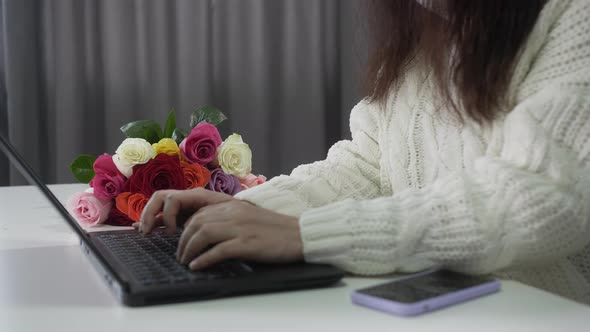 Female Hands Typing on Laptop Keyboard and Colorful Rose Bouquet Lying on Background alt