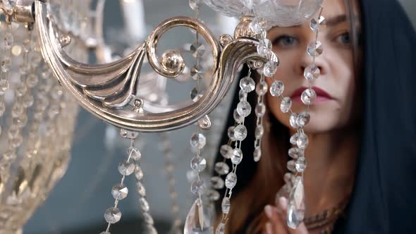 Mysterious Woman with Black Hood Playing with Luxury Shiny Chandelier Looking at Camera alt
