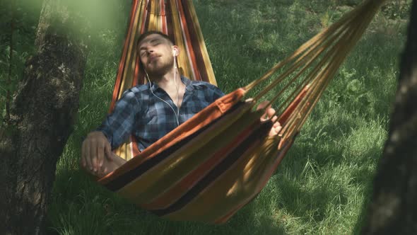 Male freelancer lying in hammock, relaxing and listening to music in earphones. Relax in hammock alt