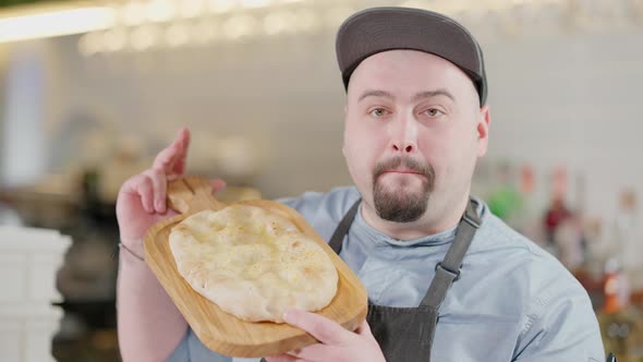 Portrait of Positive Caucasian Plussize Man Looking at Camera Smelling Delicious Baked Pinza alt