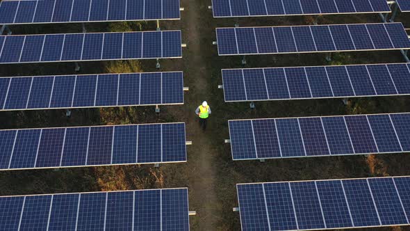 Aerial drone view technician walking between solar panels row alt