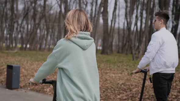 A Beautiful Couple of Young People Ride in the Park on Electric Scooters alt