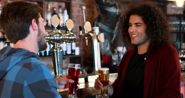 Friends interacting while toasting glasses of beer at bar counter alt