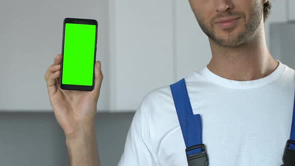 Attractive repairman demonstrating greenscreen smartphone to camera alt