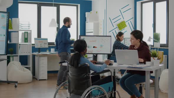 African Paralysed Woman in Wheelchair and Colleague Analyzing Reports Laptop alt