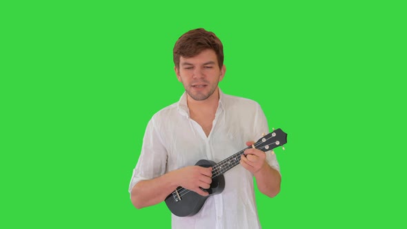 Young Man Playing Ukulele and Signing While Walking on a Green Screen, Chroma Key. alt