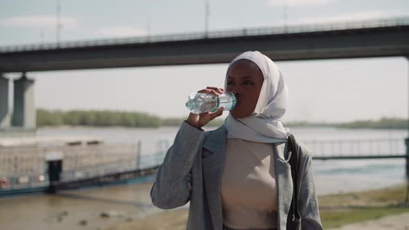 Young Black Arabian Woman Drinks Bottled Water at Riverside alt
