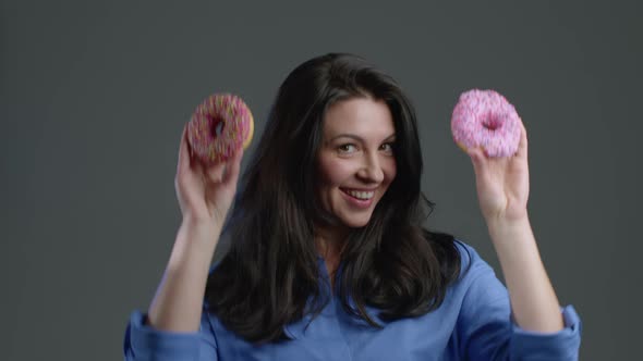 Portrait of Cheerful Adult Woman Dancing with Sweets Colorful Donuts on Grey alt