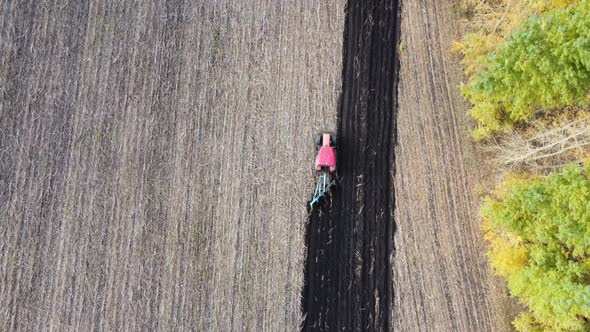 Shooting From Drone Flying Over Tractor with Harrow System Plowing Ground on Cultivated Farm Field