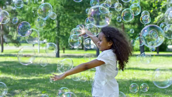Little Girl and Boy Catching Soap Bubbles while Playing Outdoor alt