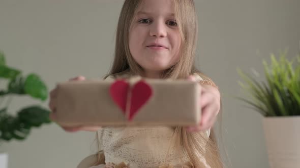 Close Up Little Girl Smiling Giving Handmade Stylish Simple Gift Box in Craft Paper at Home with alt